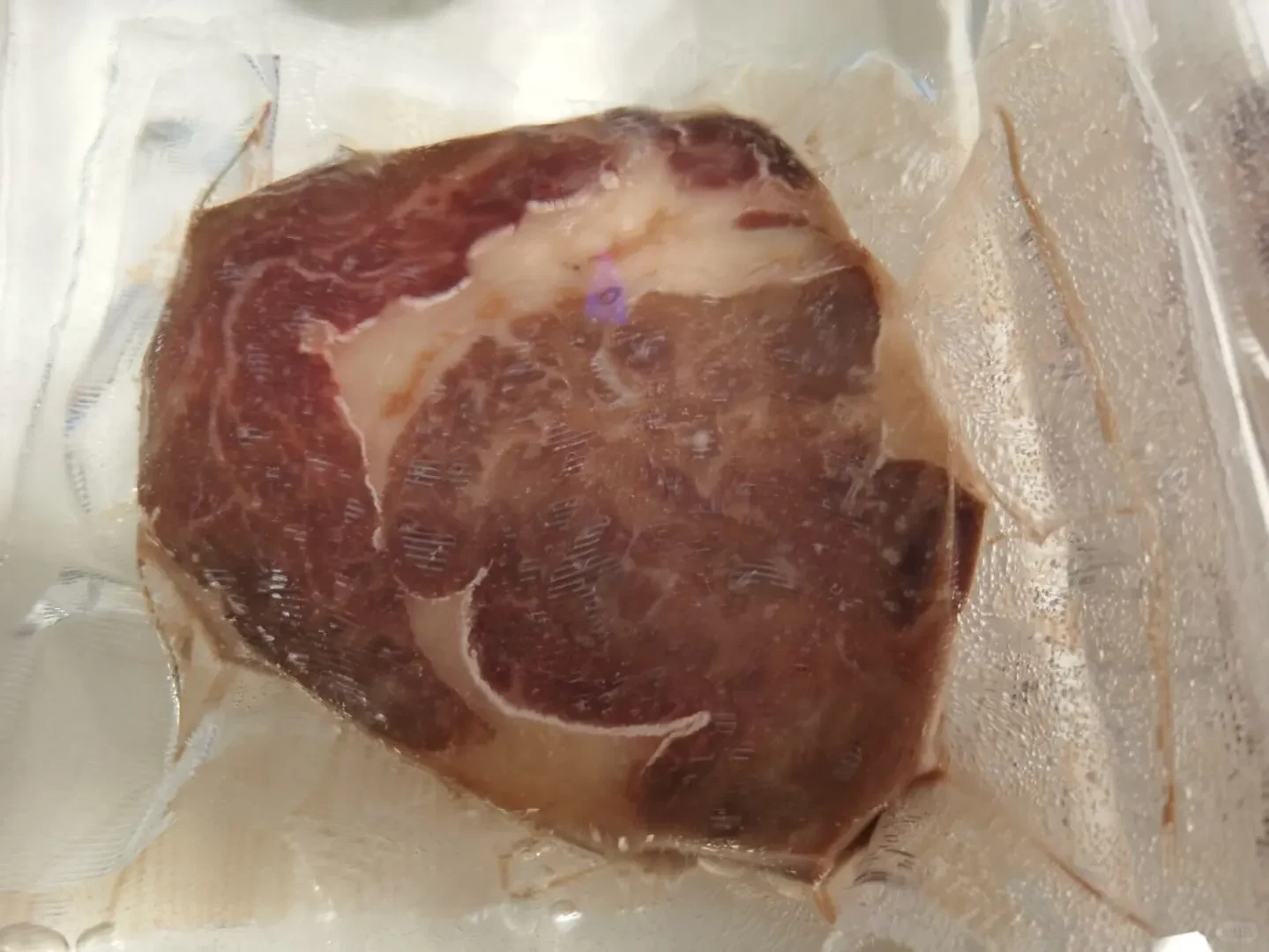 A thick cut of beef steak sealed inside a transparent vacuum bag.