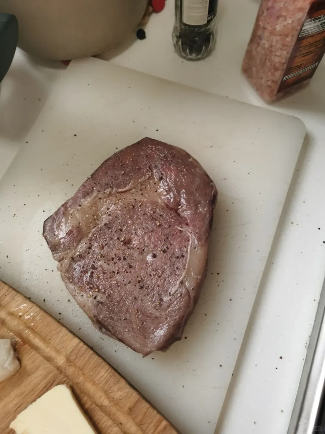 A thick-cut steak seasoned with coarse black pepper resting on a white cutting board after being cooked sous-vide.
