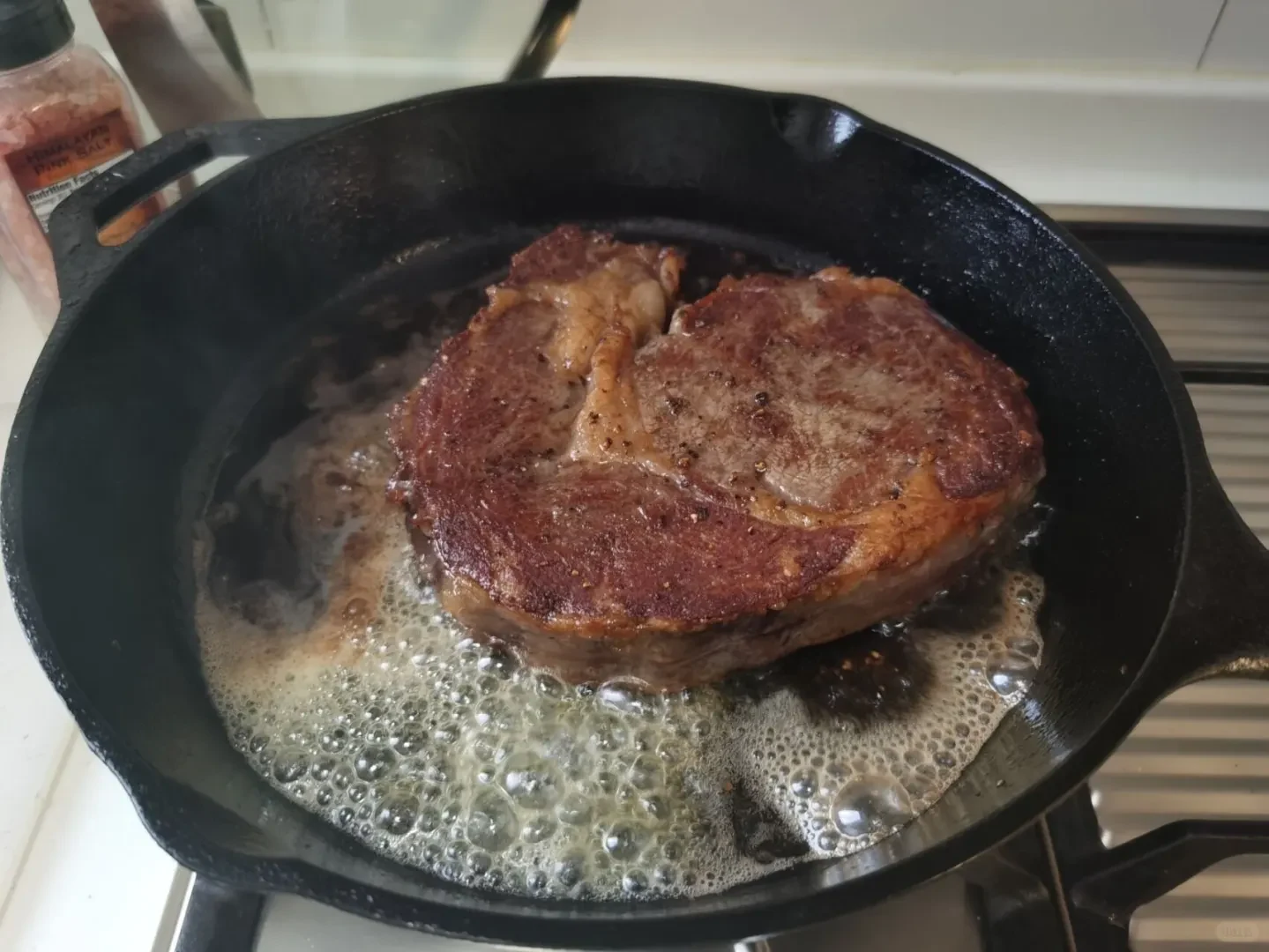 A thick cut of steak searing in bubbling melted butter within a black cast iron skillet on a stovetop.