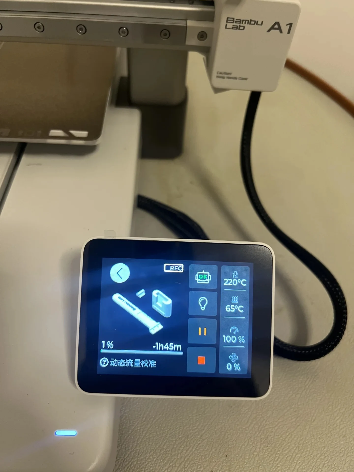 Touchscreen display on a Bambu Lab A1 3D printer showing print progress at 1% with active calibration status, positioned below the printhead and gantry.