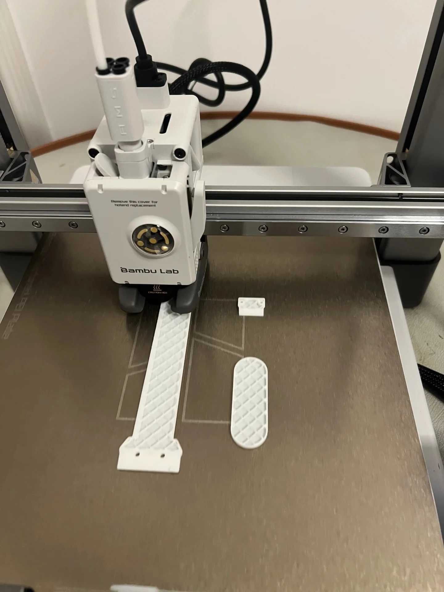 High-angle view of the Bambu Lab A1 toolhead extruding white filament onto a textured PEI build plate during a 3D printing job.