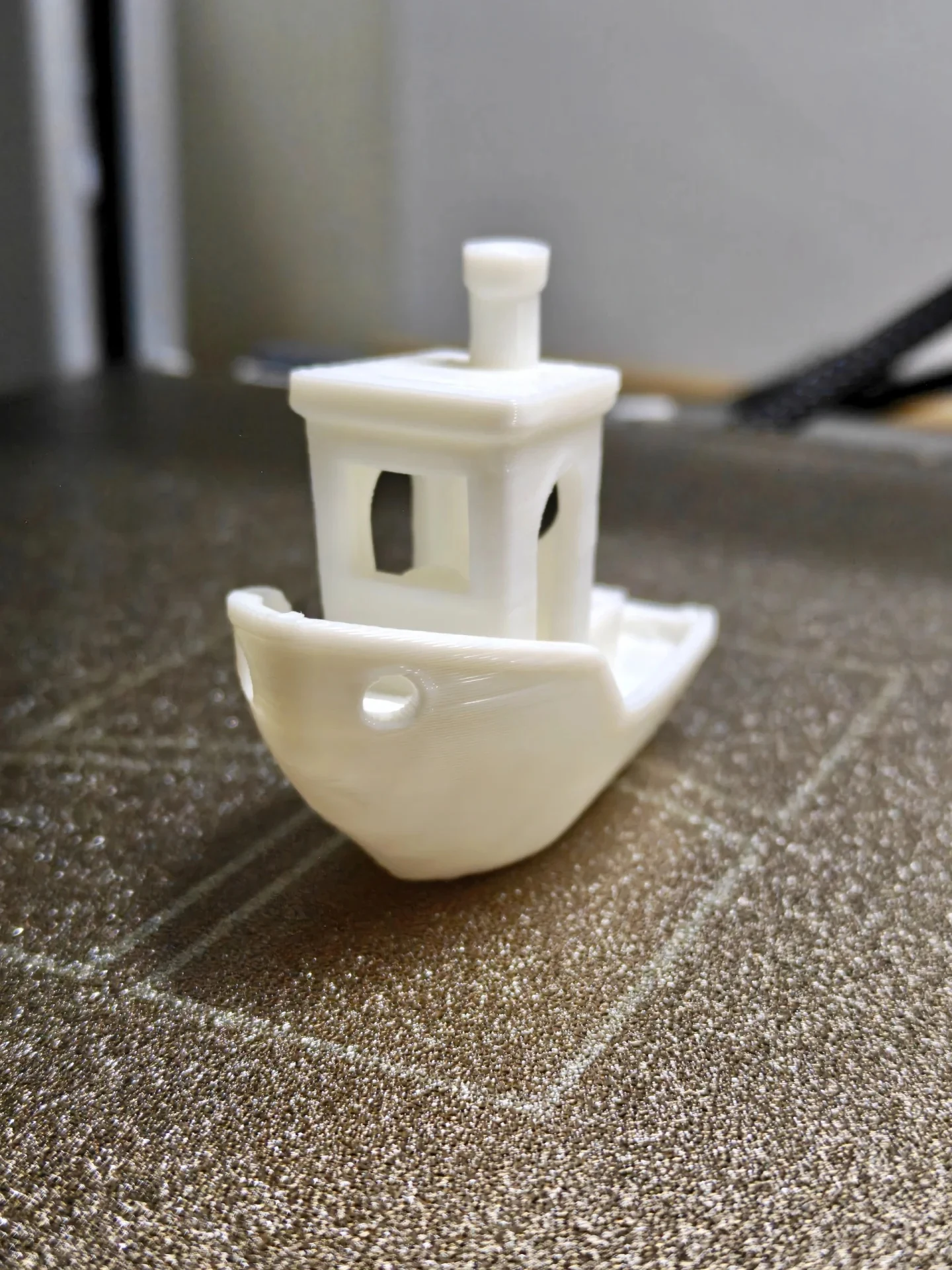 A white 3D-printed benchmark boat resting on the textured gold-toned build plate of a 3D printer.