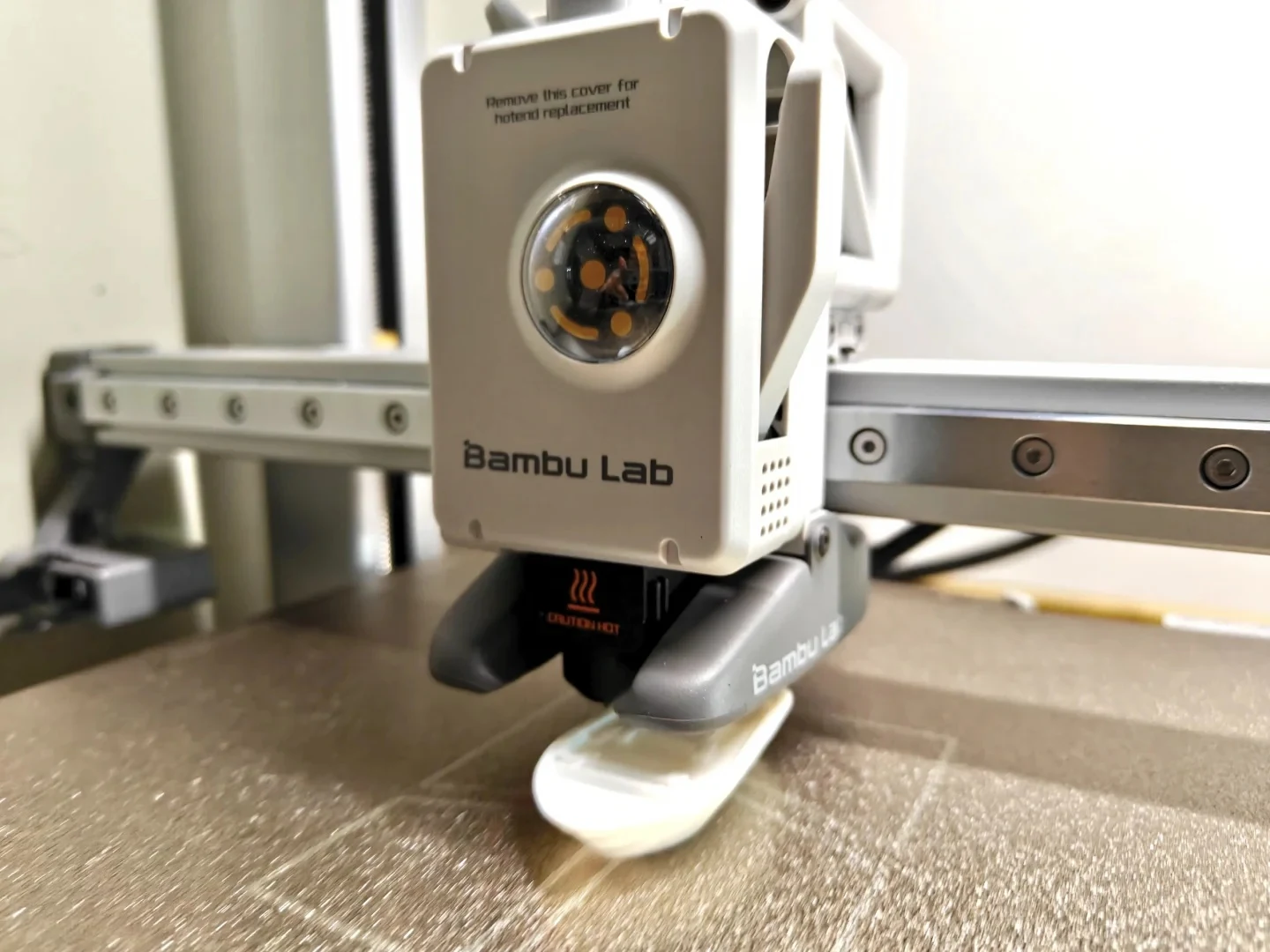 Close-up of the Bambu Lab A1 print head printing the hull of a white test boat on the textured build plate.
