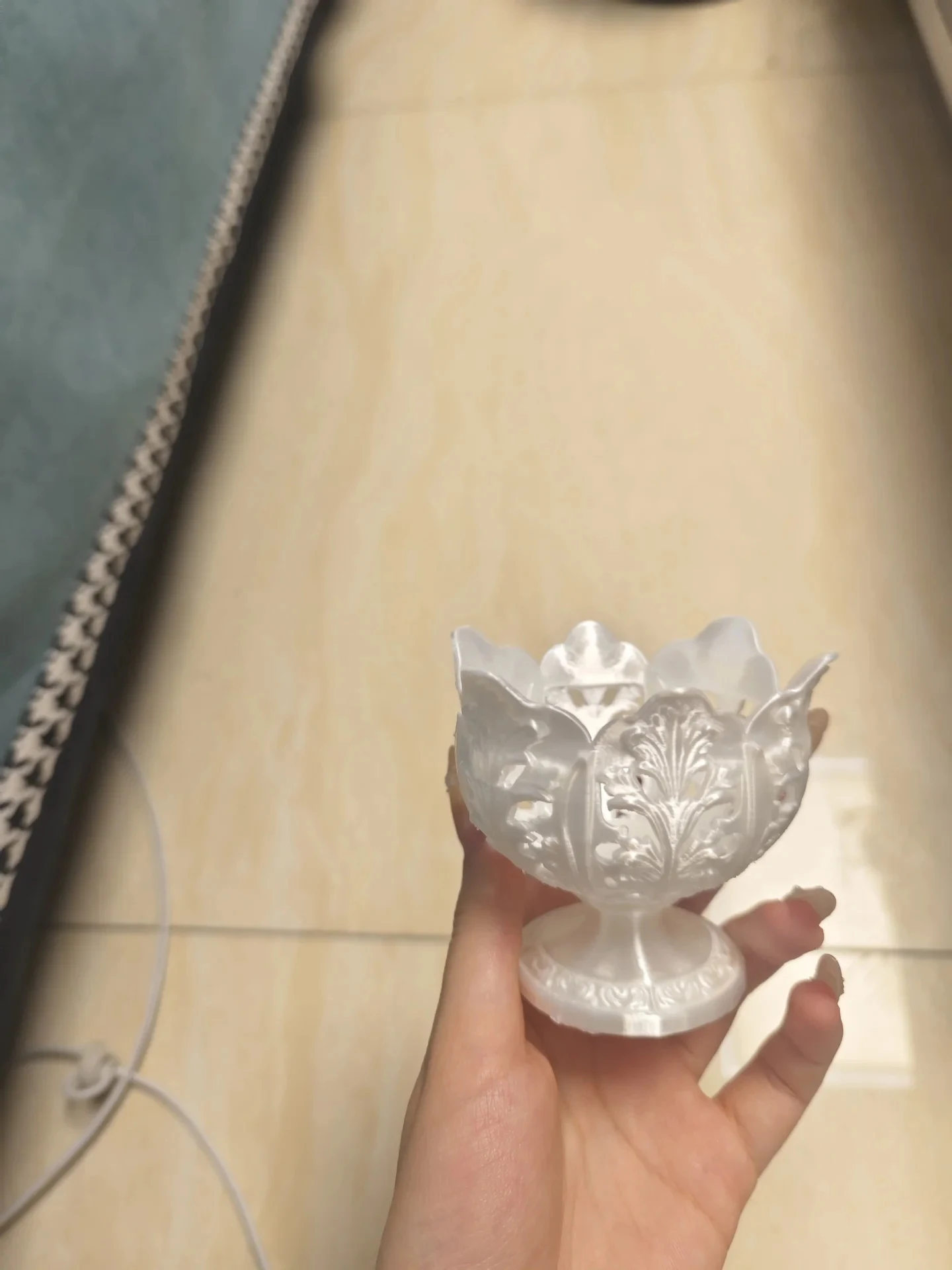 A hand holds an ornate small decorative chalice with a glossy white finish, detailed filigree openwork, and a petal-shaped rim.