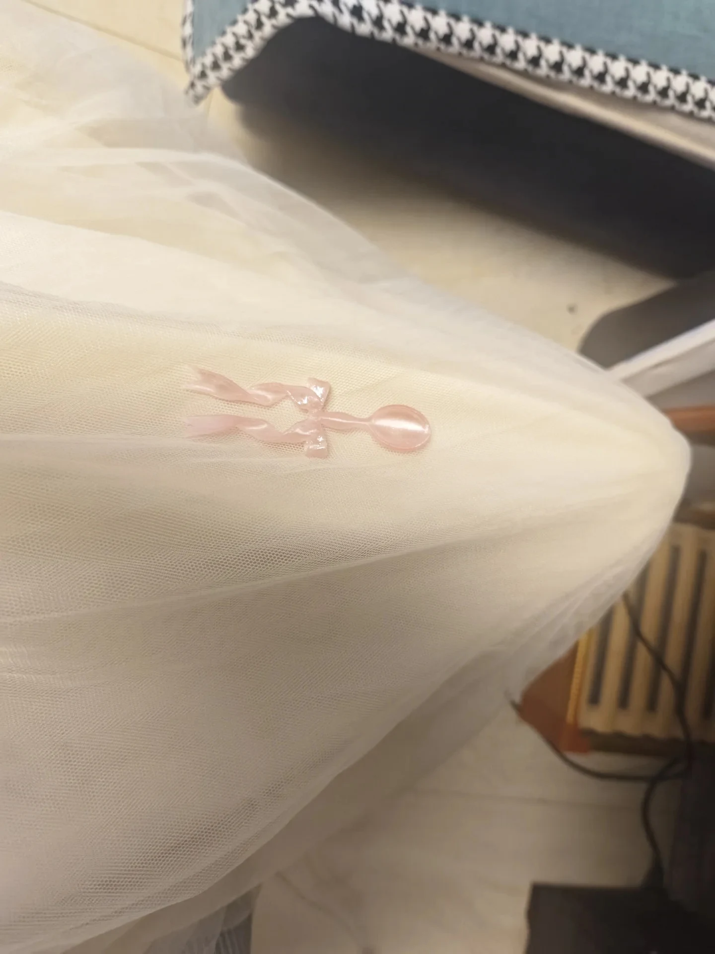 A small translucent pink 3D-printed decorative spoon with a ribbon-bow handle resting on white tulle fabric.