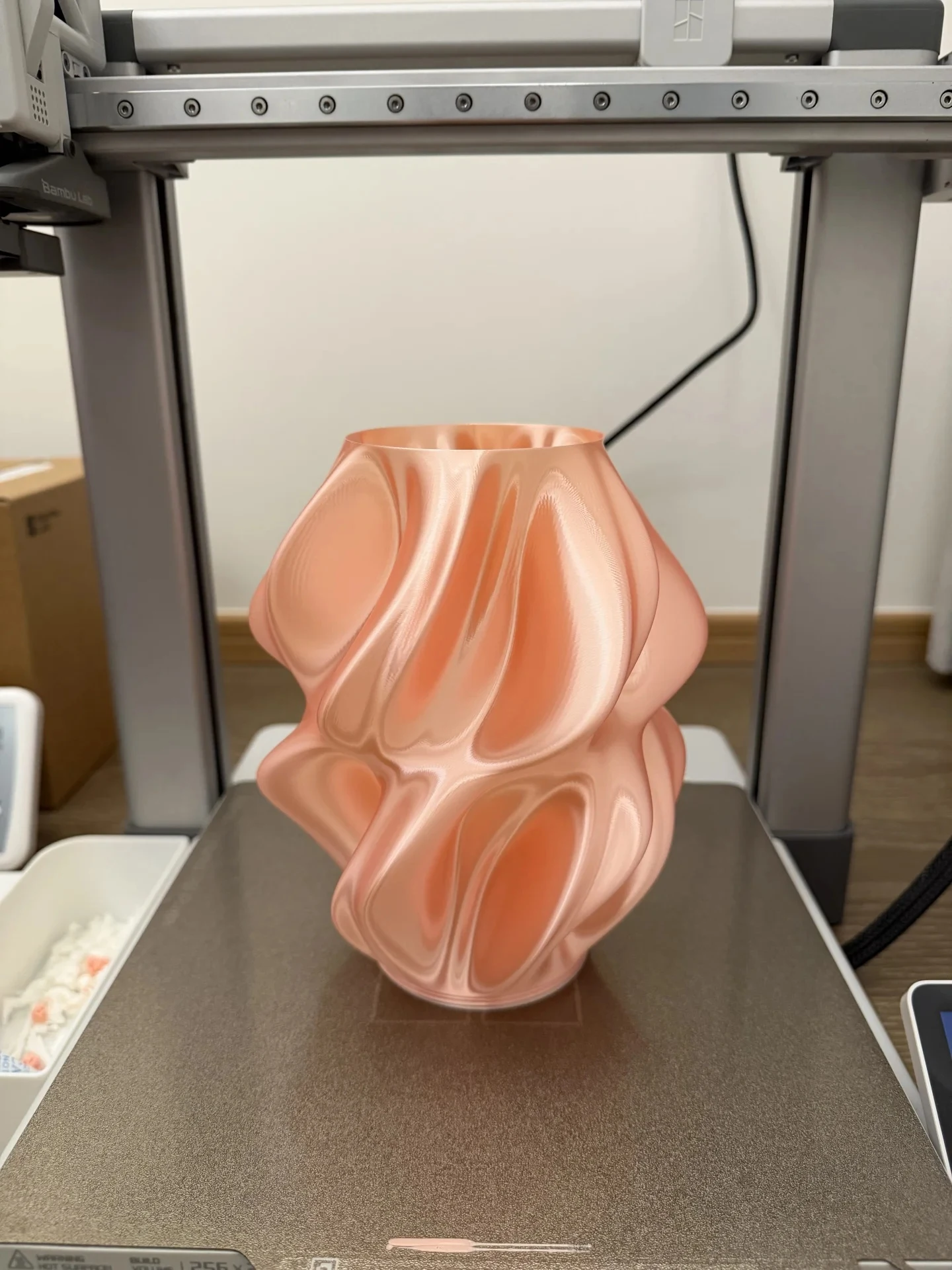 A freshly printed twisted organic lamp shade in silk pink PLA resting on the textured build plate of a Bambu Lab A1 3D printer.