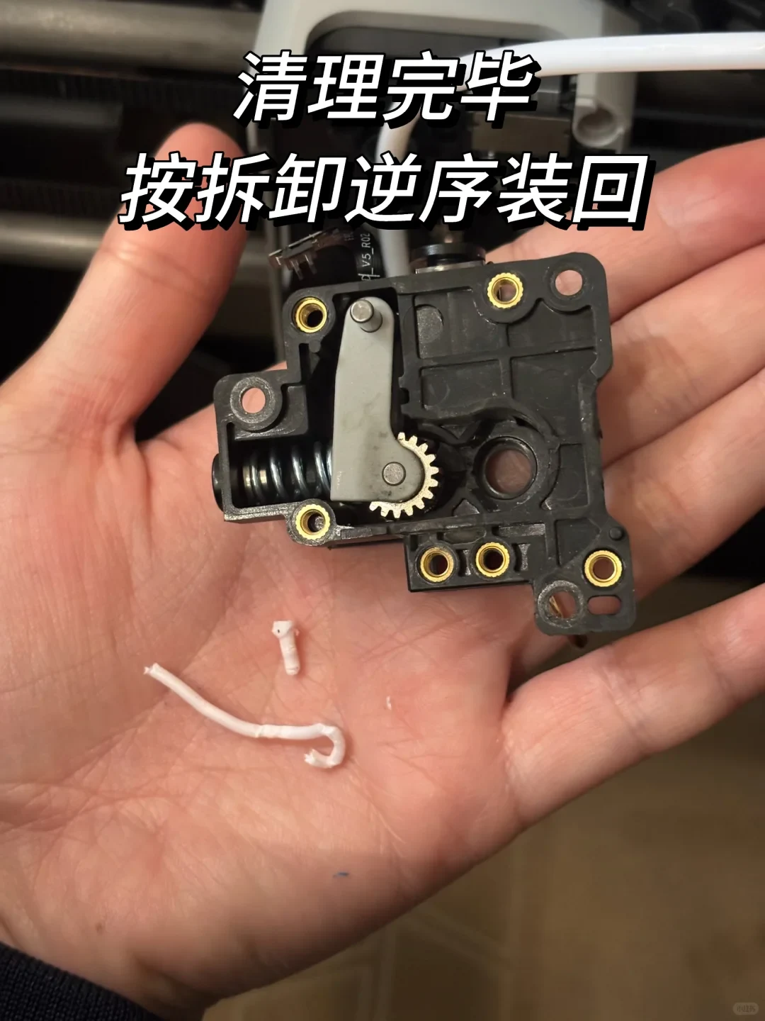 A disassembled black 3D printer extruder assembly resting on an open palm alongside small broken pieces of white filament.