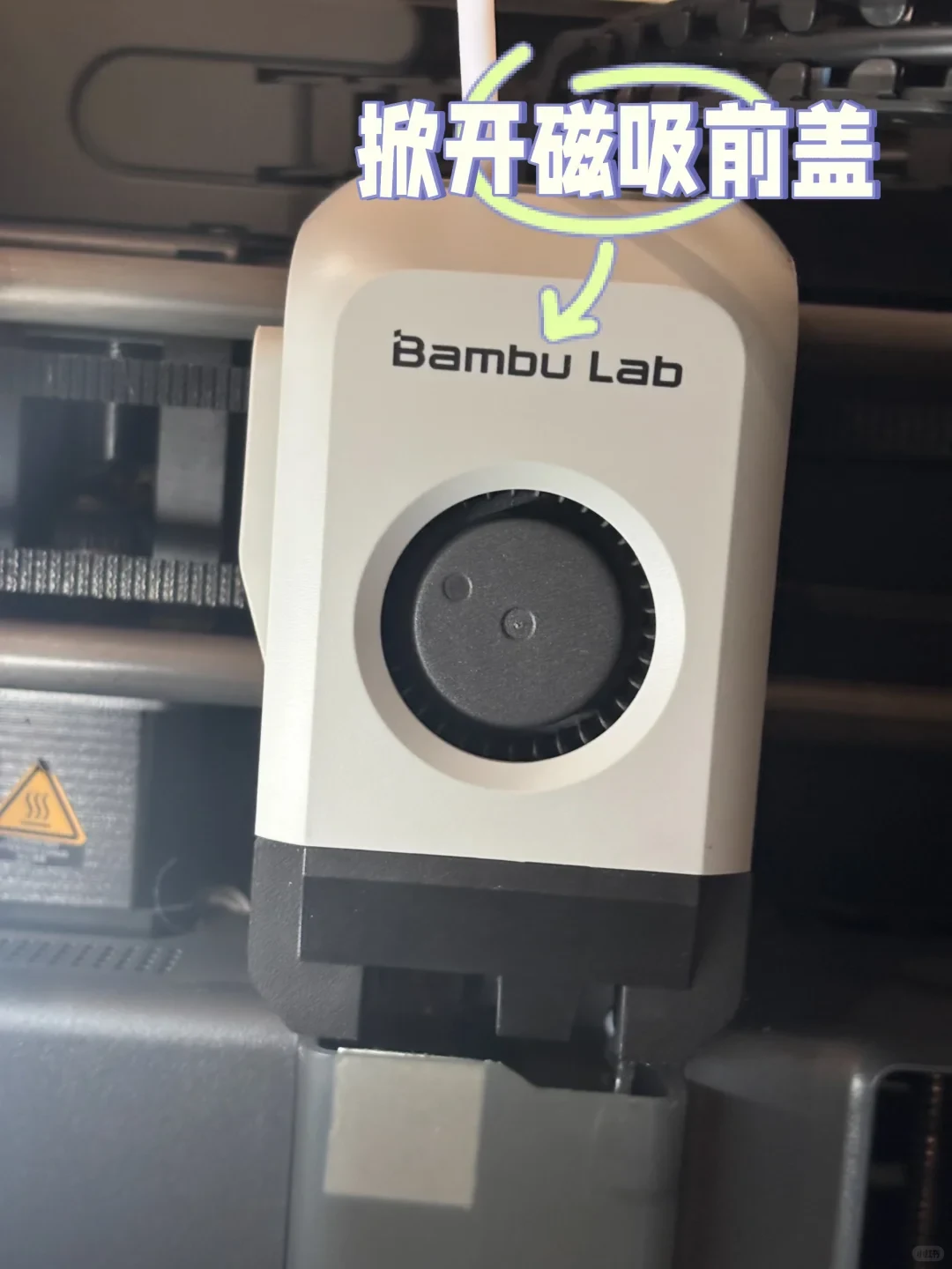 Close-up of a Bambu Lab 3D printer toolhead assembly with an arrow pointing to the front cover.