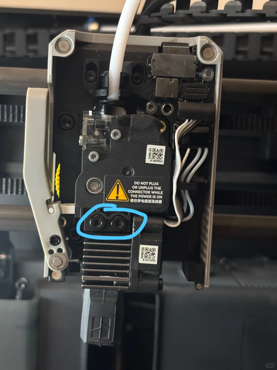 A close-up view of an opened 3D printer toolhead assembly, showing the extruder, heatsink, wiring, and two mounting screws circled in light blue.