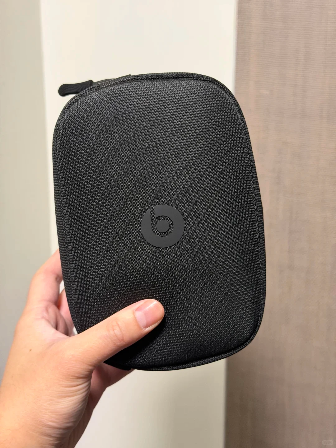 A hand holding a black woven fabric zippered Beats headphone case featuring the Beats logo in the center.