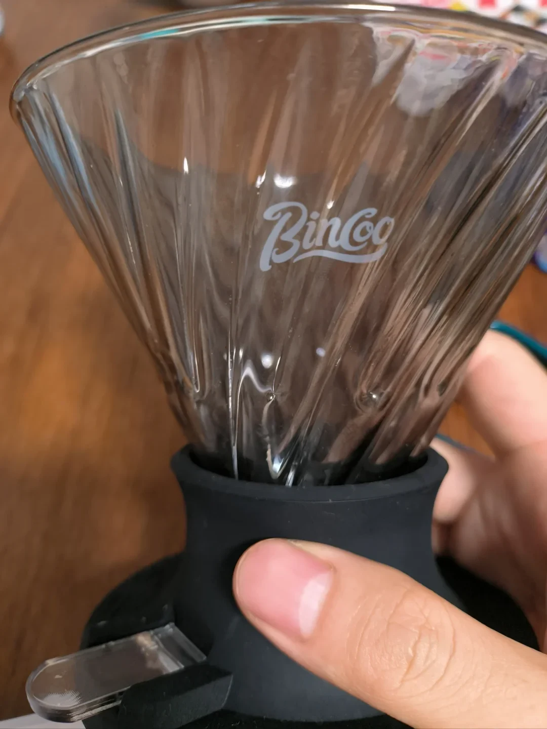 Close-up of a Bincoo-branded fluted glass immersion dripper held by its black base, with a clear manual trigger projecting from the side.