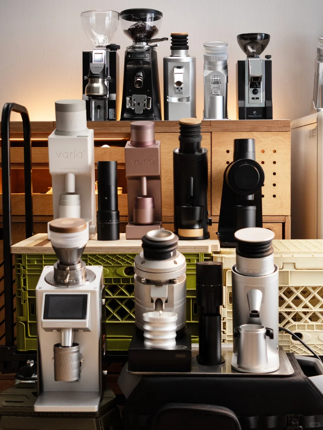 A crowded display of coffee grinders and espresso equipment, with rows of machines in different sizes, shapes, and colors on wooden shelving and a counter.