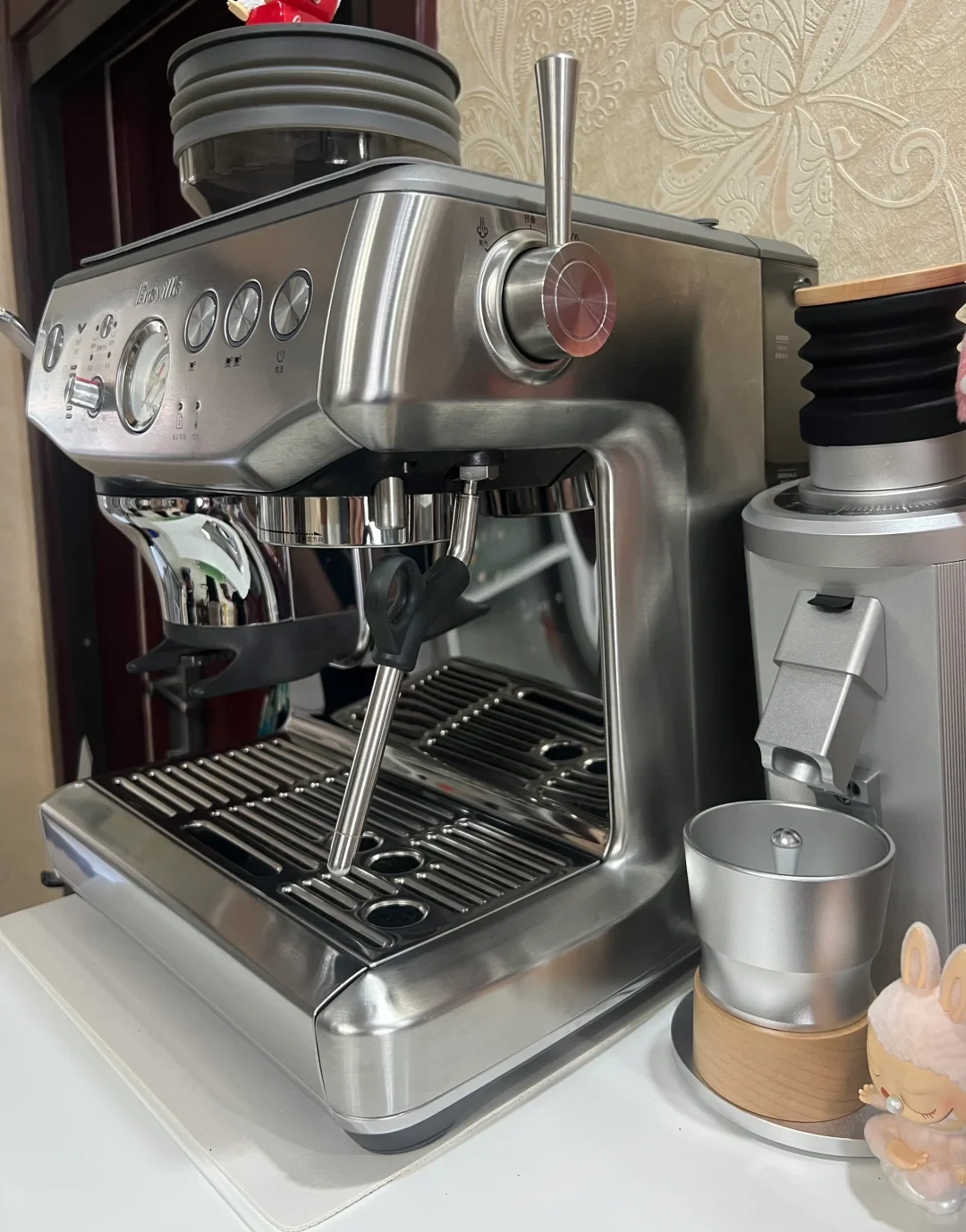 A stainless steel Breville espresso machine with an aftermarket single-dose bellows hopper and custom steam lever, standing on a counter beside a silver electric coffee grinder with a dosing cup.