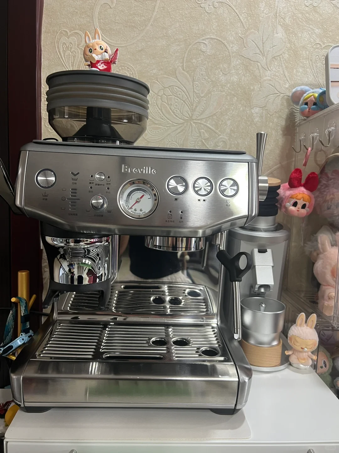 A stainless steel Breville espresso machine sits on a counter alongside a standalone coffee grinder, with several collectible bunny figurines displayed nearby.