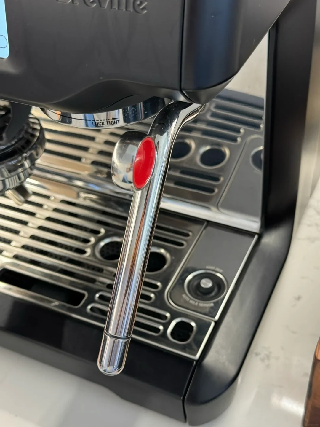 Close-up view of the chrome steam wand with an orange pull ring on a Breville espresso machine positioned above the drip tray.