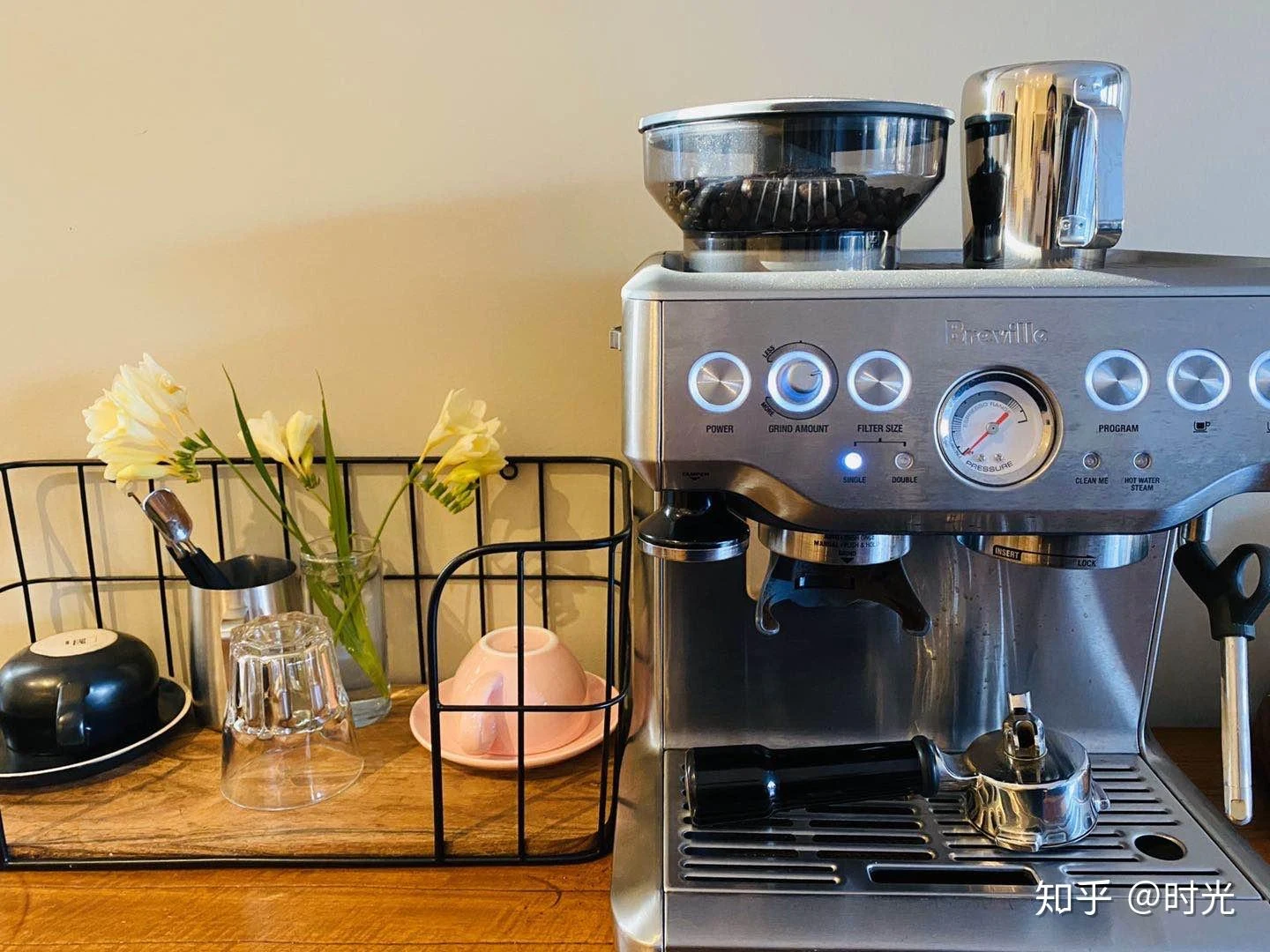 A stainless-steel Breville BES870 espresso machine with an integrated grinder, coffee beans in the hopper, a pressure gauge, portafilter, and steam wand on a wooden counter.