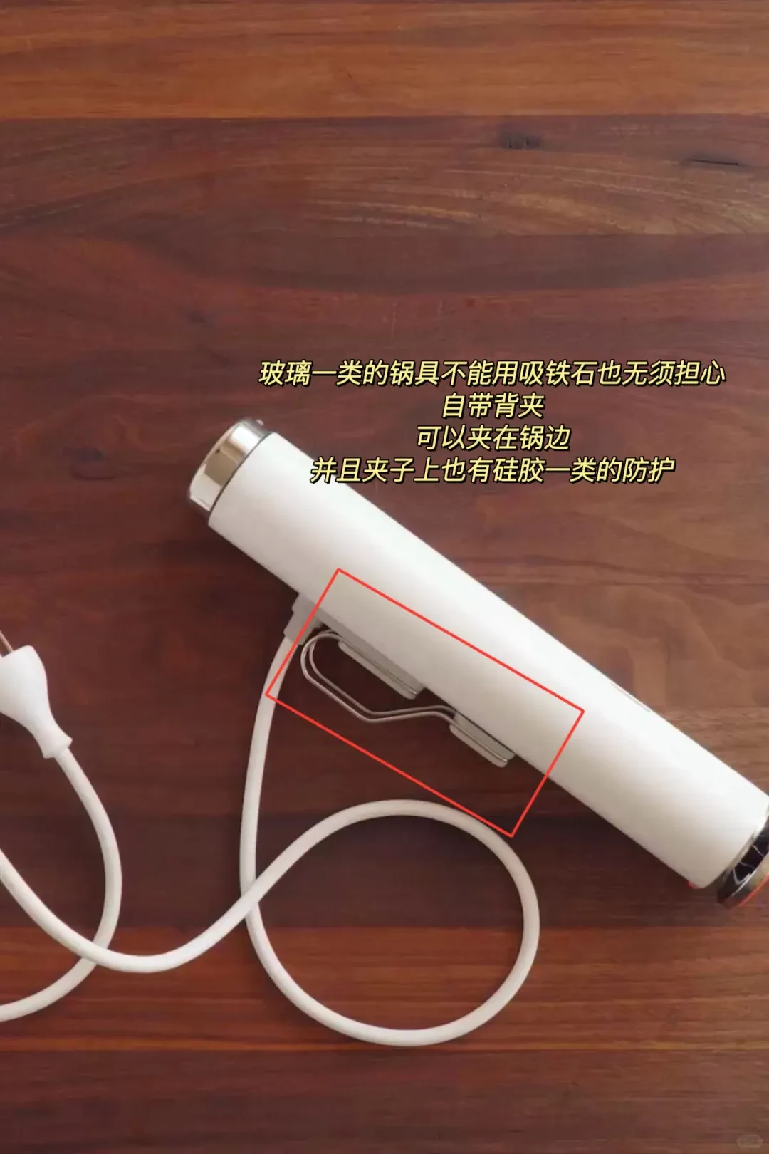 A white immersion cooking wand with a white power cord rests diagonally on a wooden surface, featuring a red rectangle highlighting the metal mounting clip along its side, accompanied by Chinese descriptive text above it.