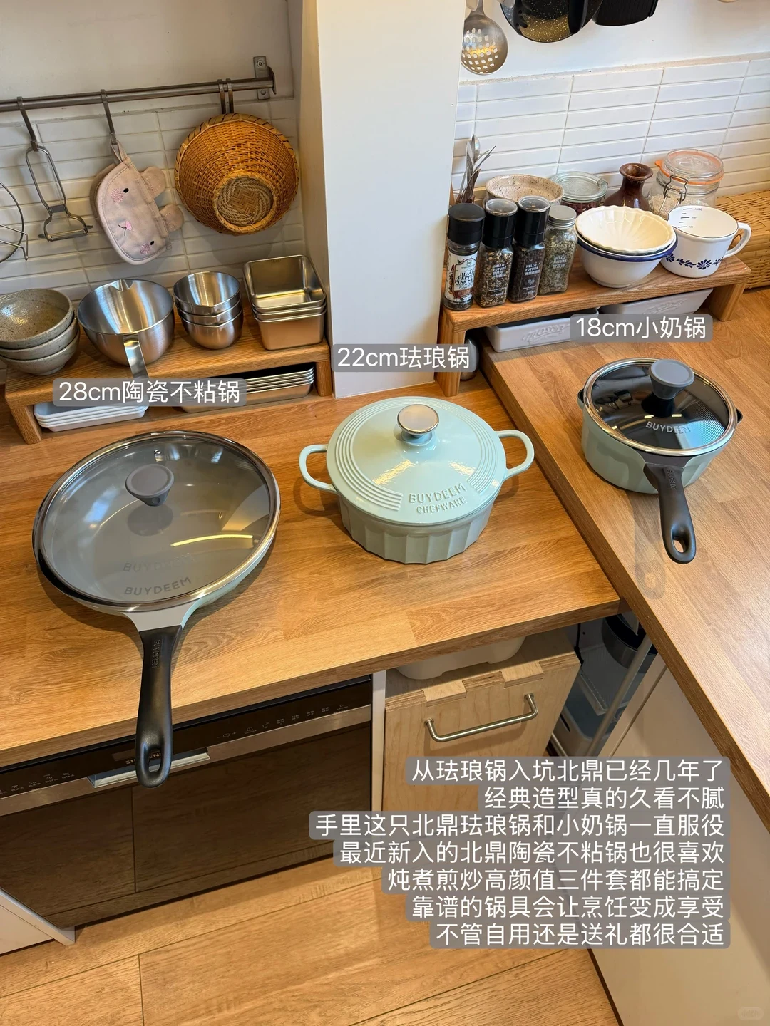 Three pale mint-green cookware pieces by Buydeem set on a wooden kitchen countertop, including a 28 cm ceramic non-stick skillet, a 22 cm cast iron enamel pot, and an 18 cm saucepan.
