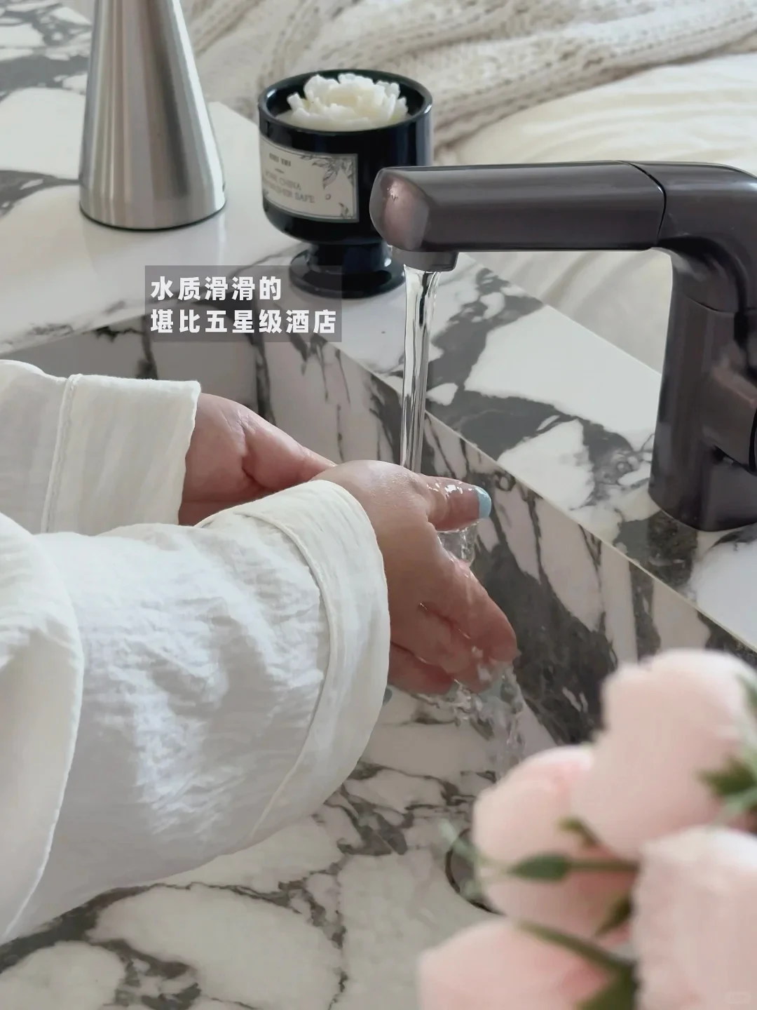 Hands cupped under running water from a dark faucet over a black and white marble sink counter.