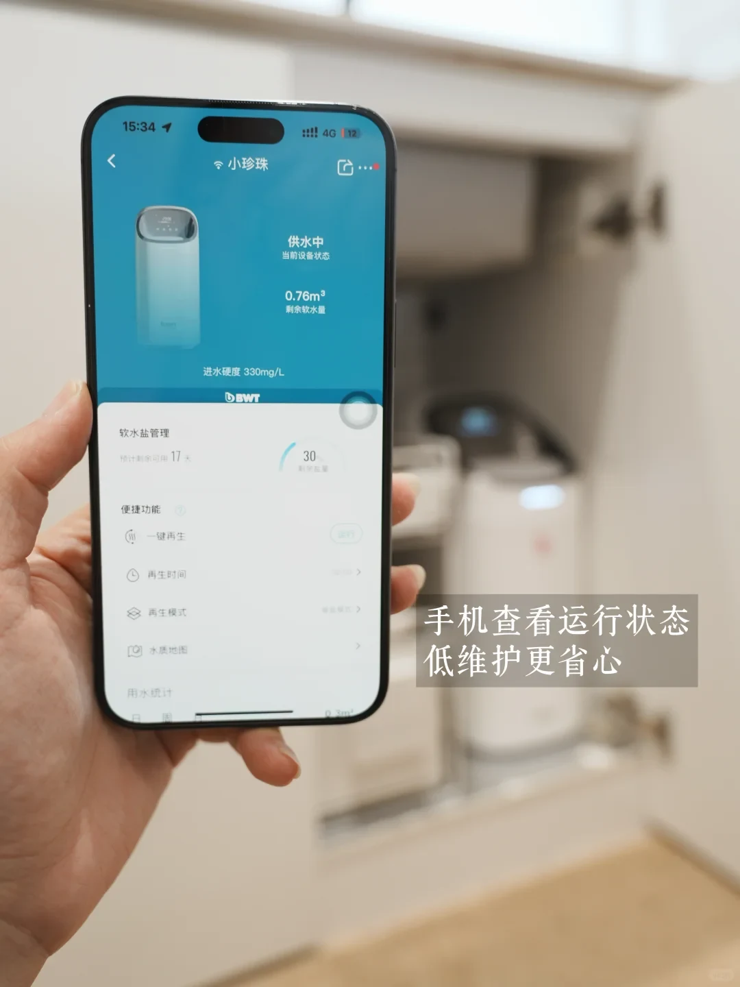 A hand holding a smartphone displaying the companion app for a BWT water softener installed inside a cabinet in the background.