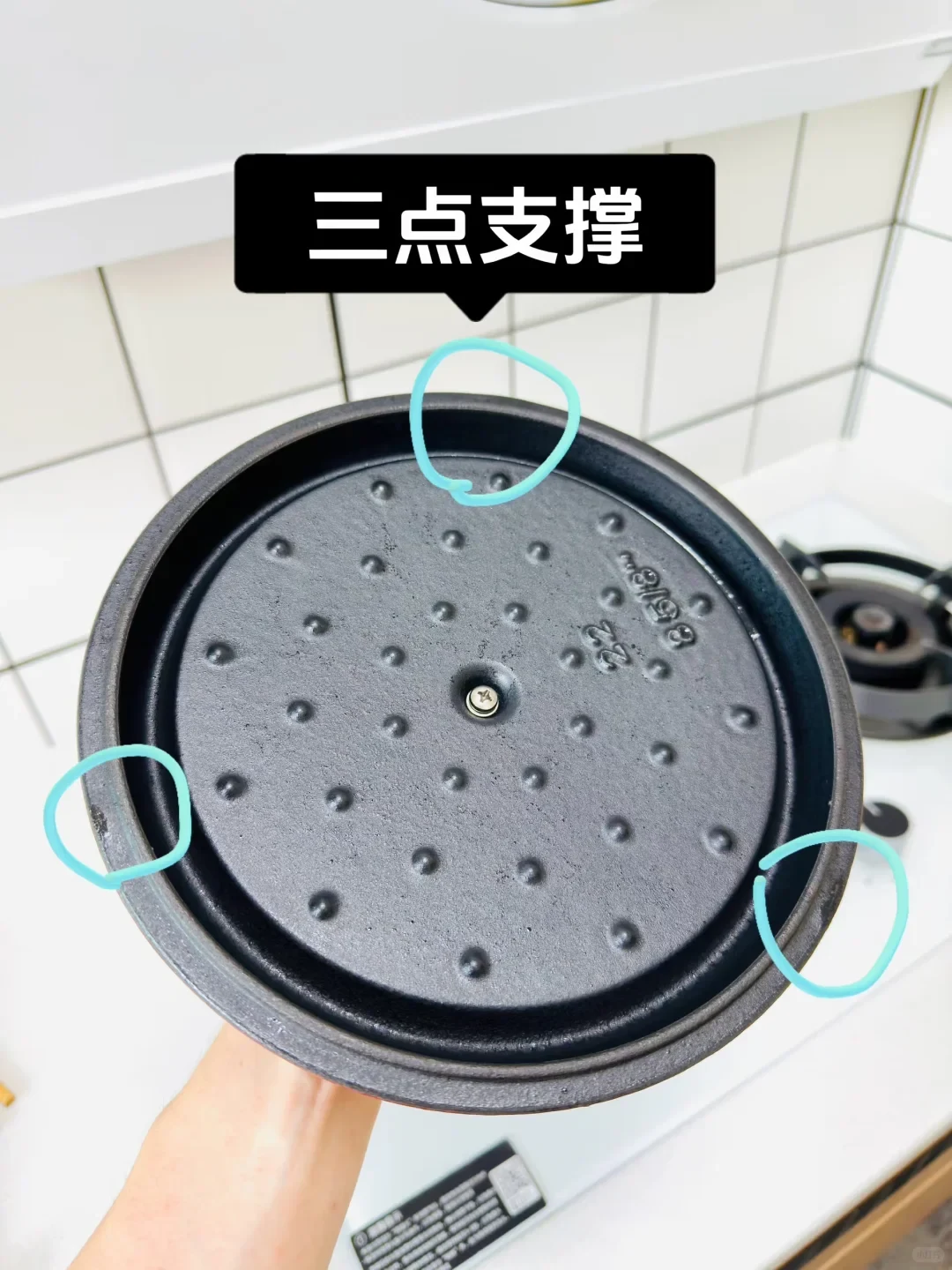 Underside of a black cast iron Dutch oven lid featuring self-basting spikes, with three blue circles highlighting support nubs along the rim beneath a text banner.