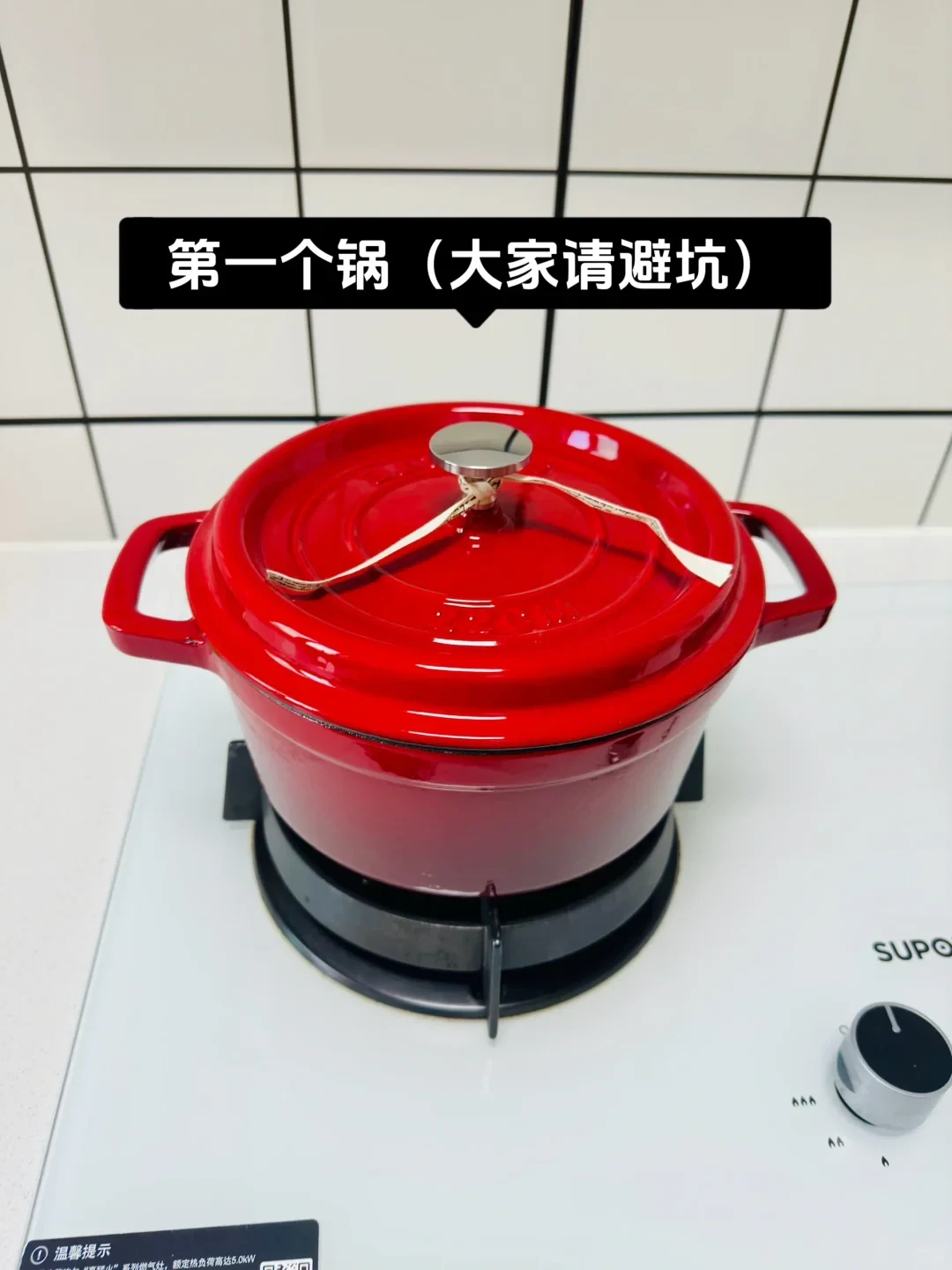 A glossy red enameled cast iron pot with a lid resting on a white gas stovetop.