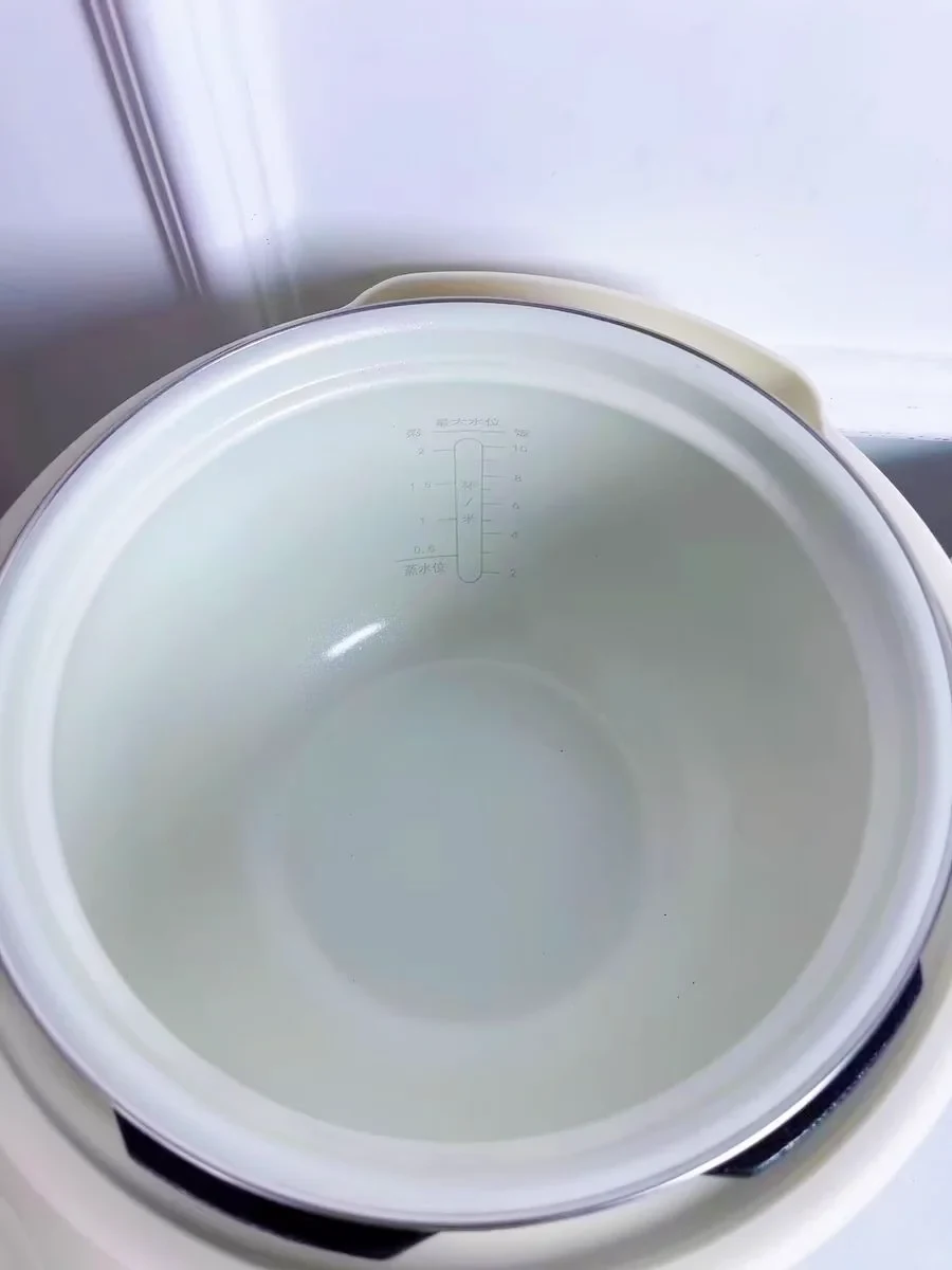 Top-down view of the interior of an electric cooker showing water and rice measurement markings printed on the inner pot.
