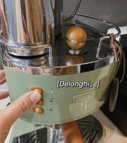Close-up of a hand pressing the top button on an olive green De'Longhi ECO310 espresso machine with a green status indicator lit.