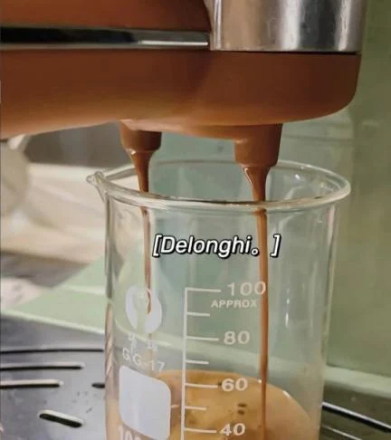 Close-up of espresso flowing from the dual spouts of an espresso machine portafilter into a glass graduated beaker, forming rich crema at the bottom.
