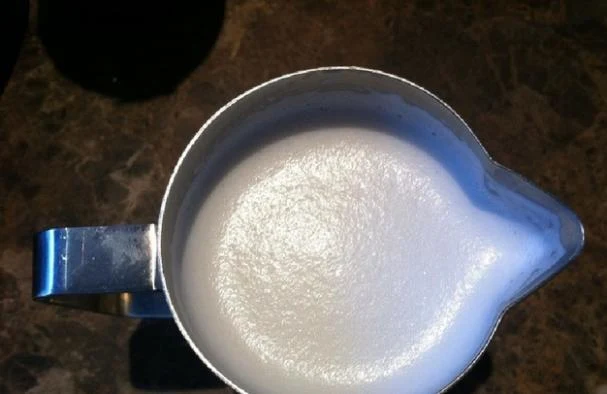 Top-down view of a stainless steel milk frothing pitcher filled with smooth white milk foam.