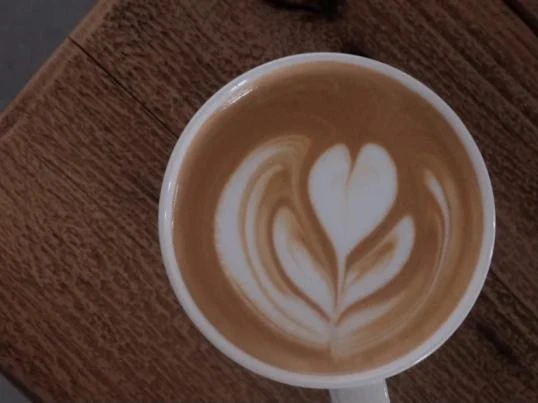 Overhead view of a cup of latte with white heart-shaped and leaf-like latte art on a wooden table.