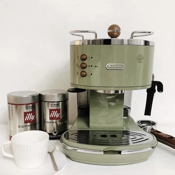 Retro pale-green De'Longhi espresso machine with a black steam wand, two illy espresso coffee cans, a white cup and saucer, and coffee tools arranged on a counter.
