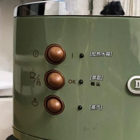 Close-up of the green De'Longhi ECO310 espresso machine control panel, showing three brown buttons with Chinese labels for heating the water tank, extraction, and steam.