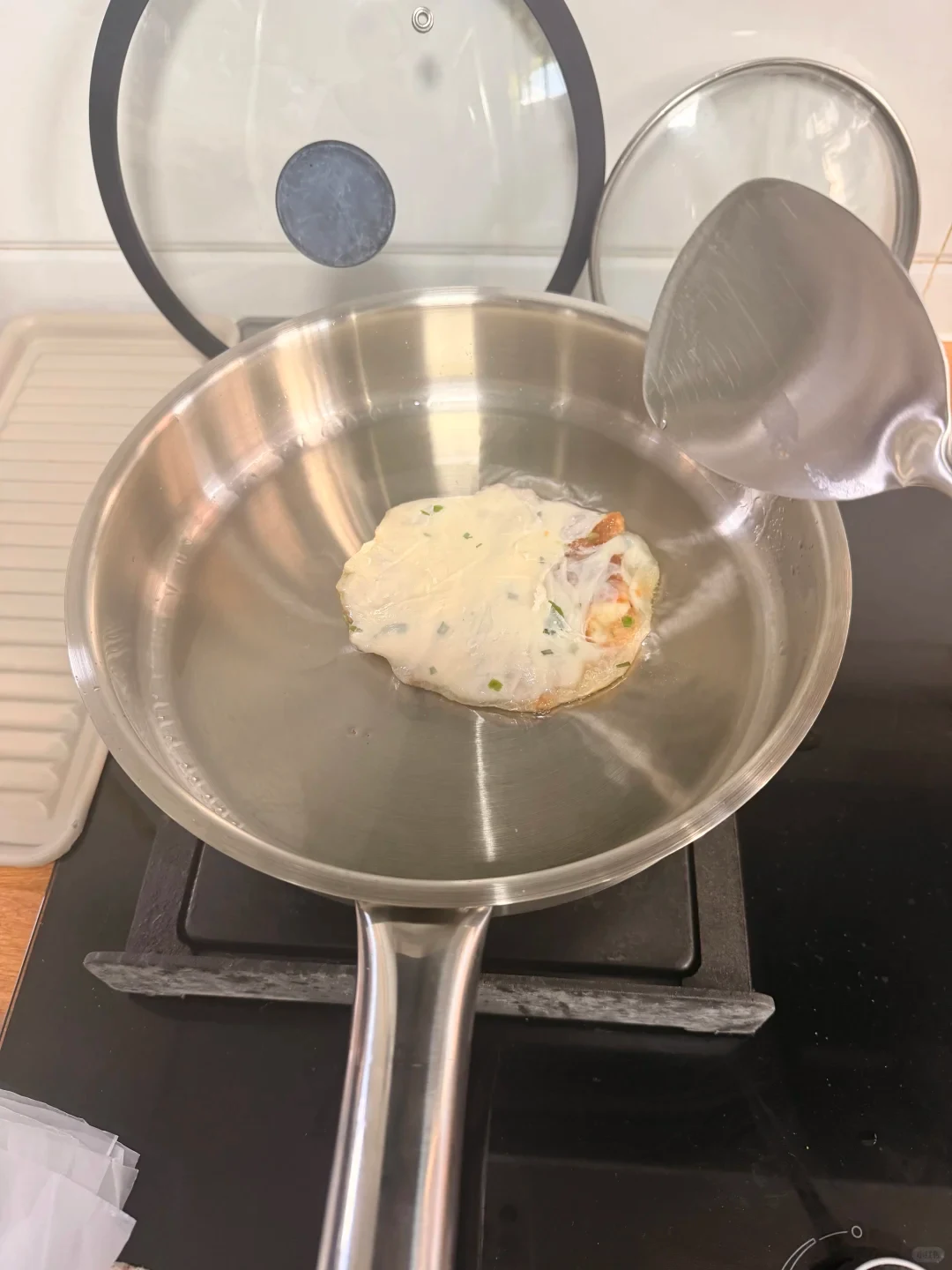A small patty cooking in a stainless steel pan, with a metal spatula nearby.