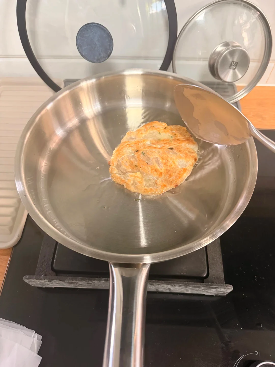 A browned small patty in a stainless steel pan, with a spatula above it.