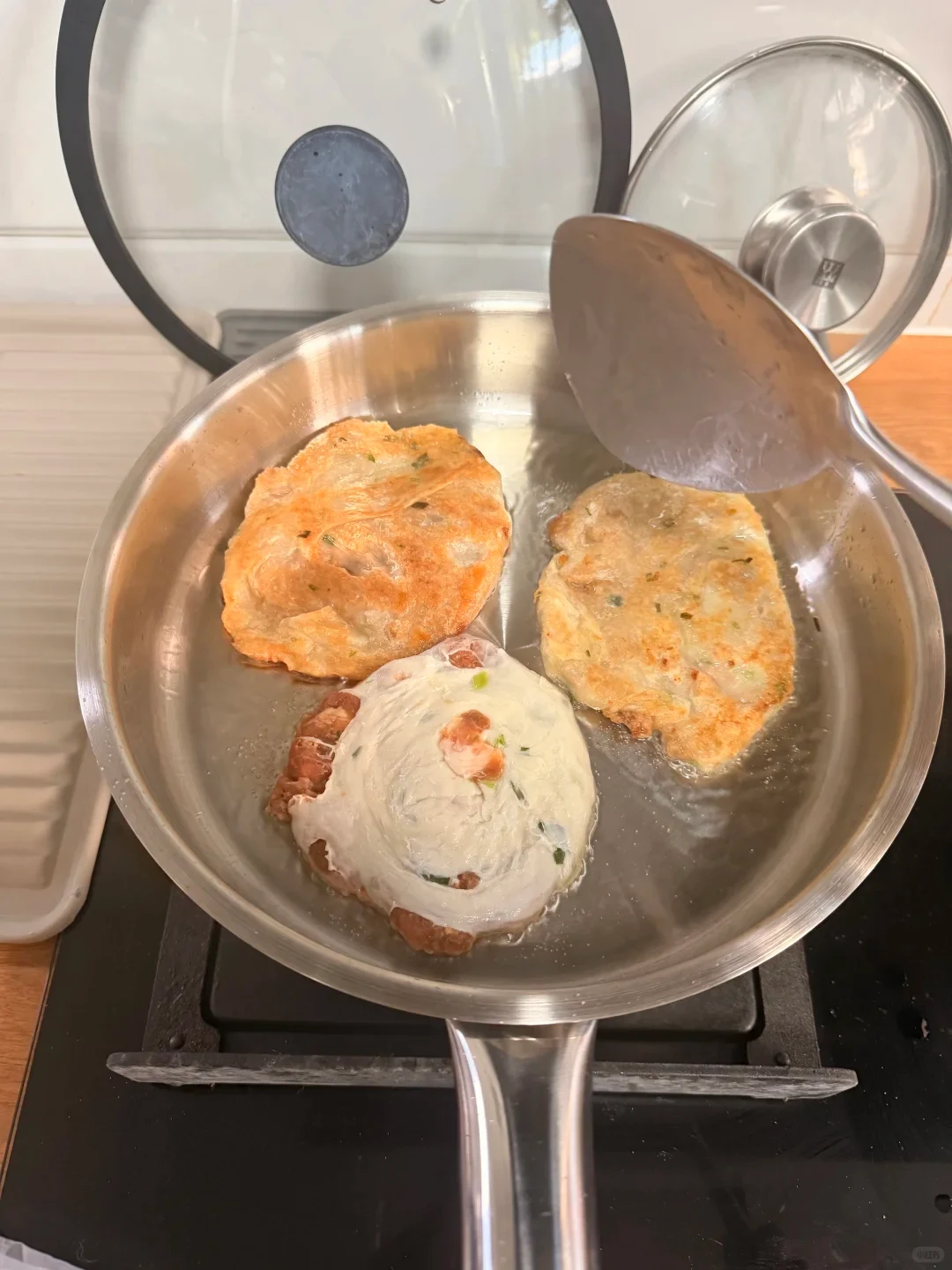 Three small patties browning in a stainless steel pan, with a spatula above them.