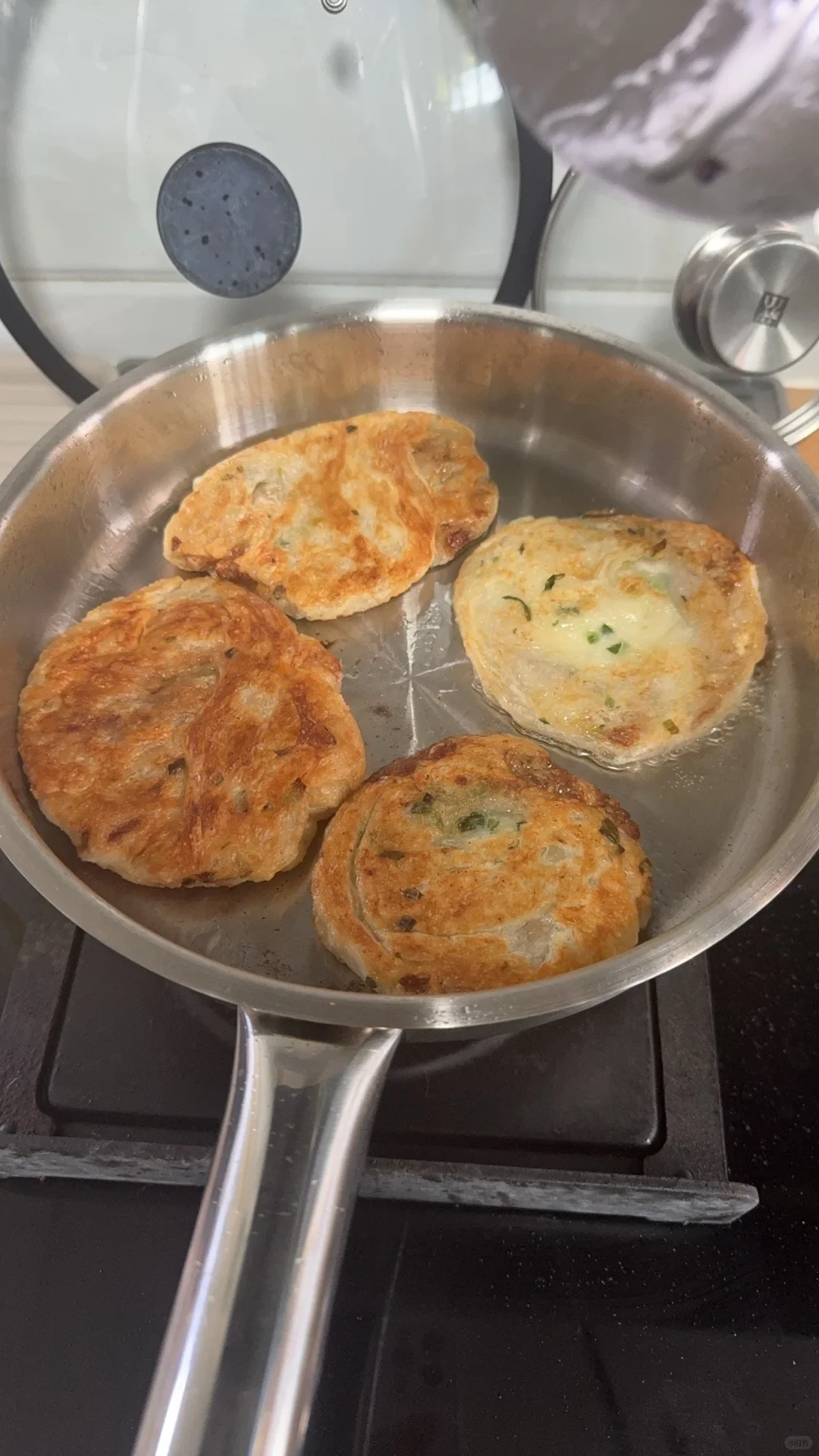 Four small patties browning together in a stainless steel pan.