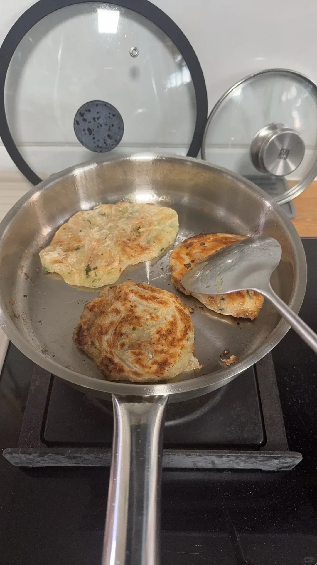 Three small patties in a stainless steel pan, with a spatula touching one.
