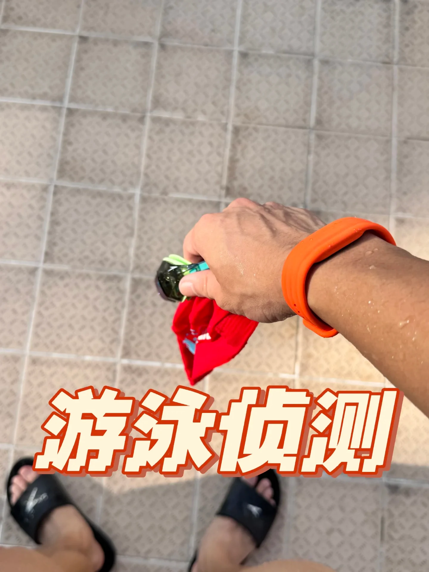 Top-down view of someone wearing an orange wristband, black slides, and holding a red swim cap and goggles against a tiled floor, with Chinese text overlaid at the bottom.
