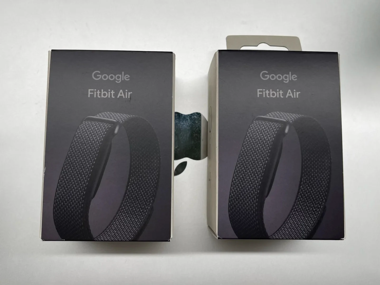 Two packaging boxes for Google Fitbit Air side-by-side, each featuring an image of a black woven fitness tracker strap against a dark background.
