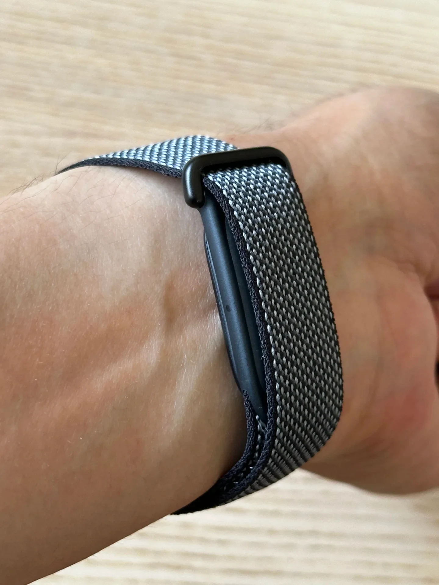 Close-up shot of a black and grey woven nylon sport loop watch band worn on a wrist, showing the matte black loop fastener.