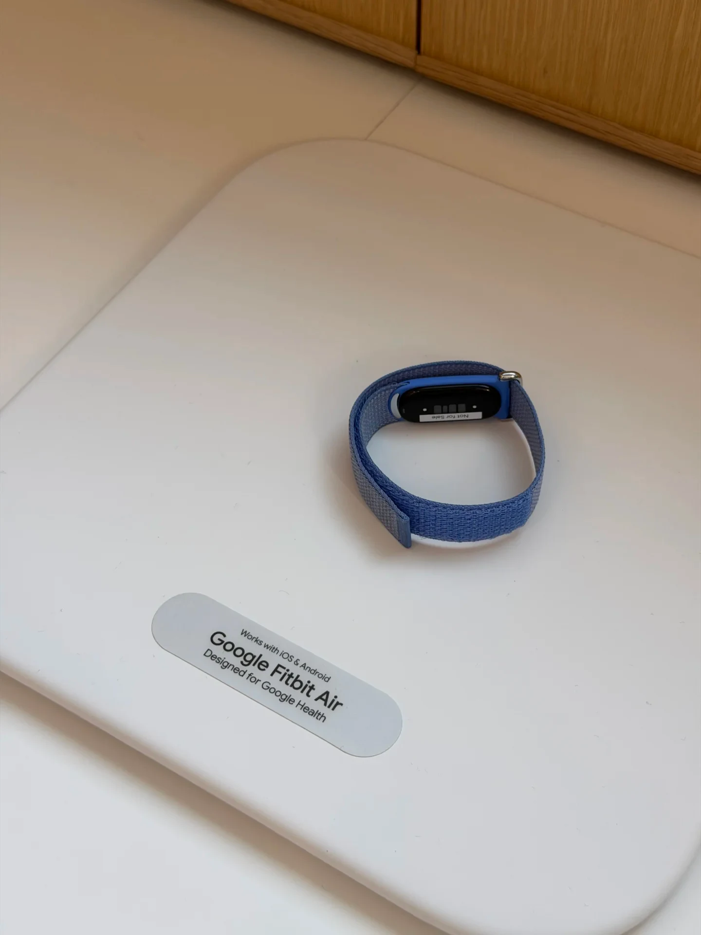 A blue wearable fitness band labeled Google Fitbit Air resting on a white display stand.