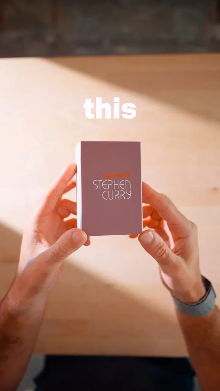 Two hands holding a small rectangular box labeled 'STEPHEN CURRY' against a wooden table, with the word 'this' floating above.