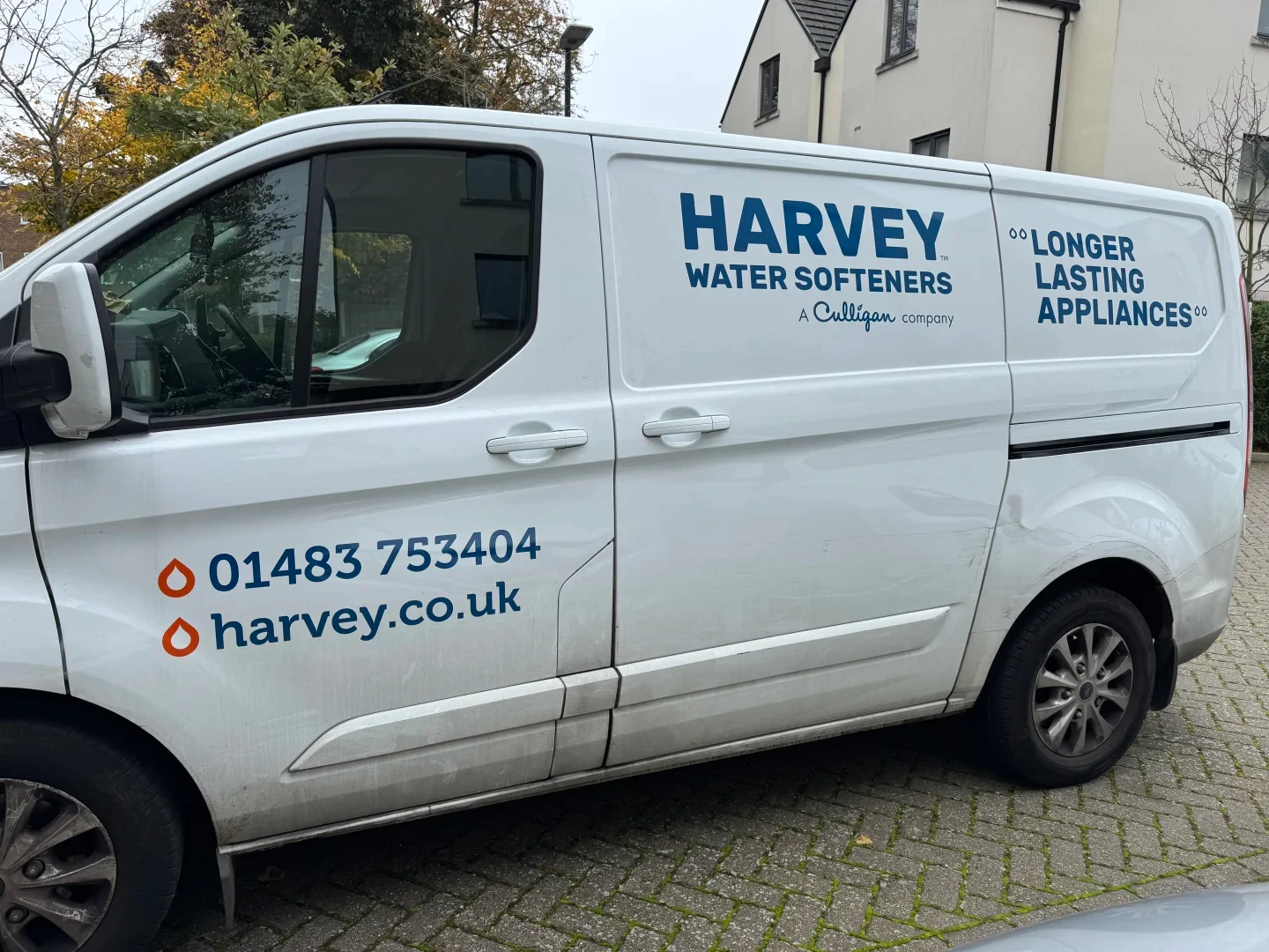 Side profile of a white Harvey Water Softeners commercial van parked on a brick-paved driveway.
