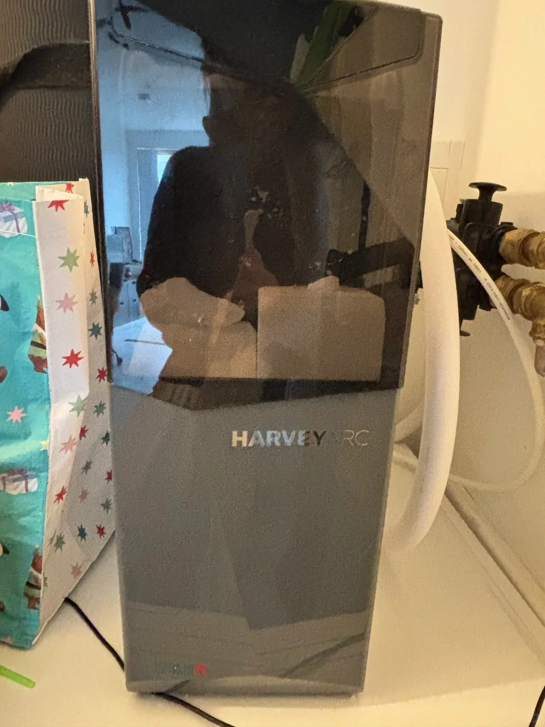 A Harvey Arc water softener unit standing inside a cabinet or utility area, featuring a grey lower body and a dark tinted semi-transparent upper cover showing internal salt blocks.