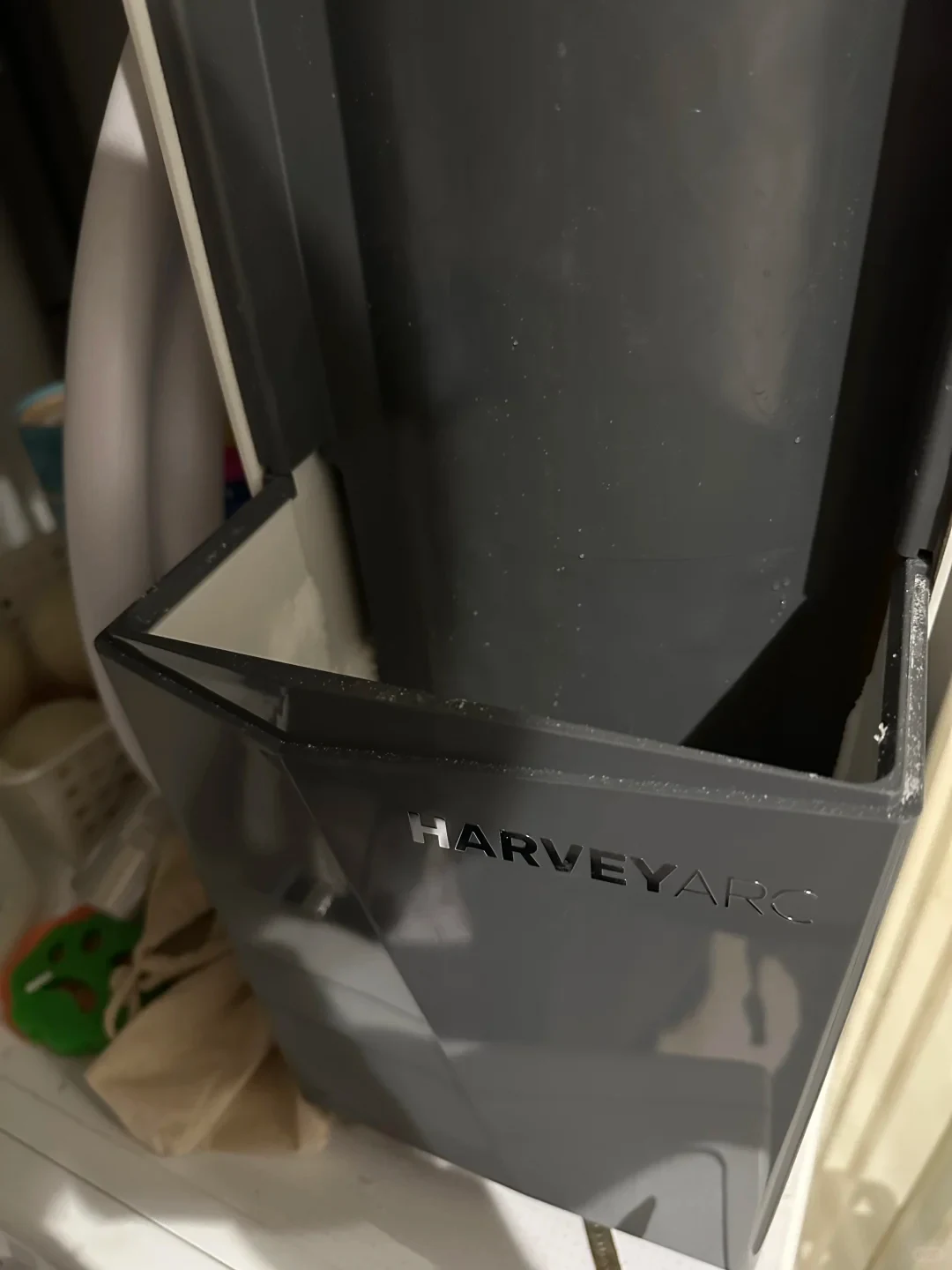 A close-up view of a dark grey Harvey Arc water softener unit with its front salt hopper open, displaying the interior compartment and the silver 'HARVEY ARC' branding on the front panel.