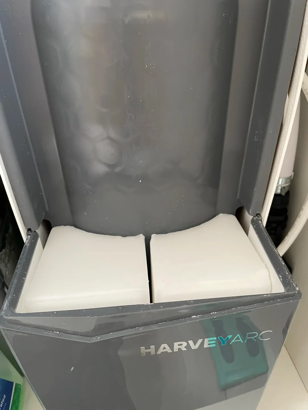 Top view of an open grey Harvey Arc water softener containing two curved rectangular white salt blocks inside its refill compartment.