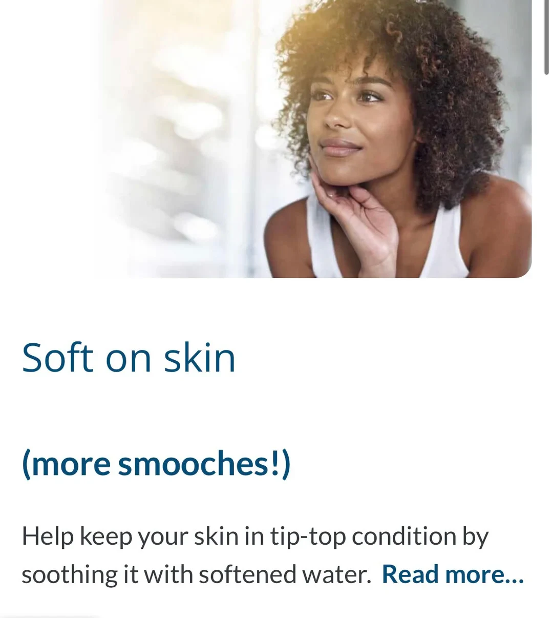 Webpage section featuring an image of a smiling woman with curly hair resting her chin on her hand, above text reading 'Soft on skin (more smooches!) Help keep your skin in tip-top condition by soothing it with softened water. Read more...'