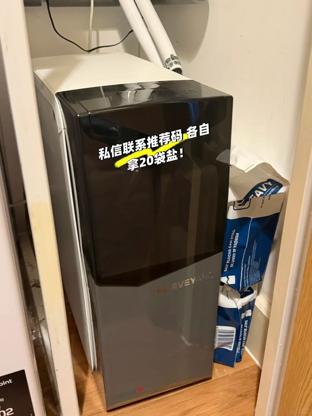A HarveyArc water softener installed inside a cabinet next to bags of salt blocks.