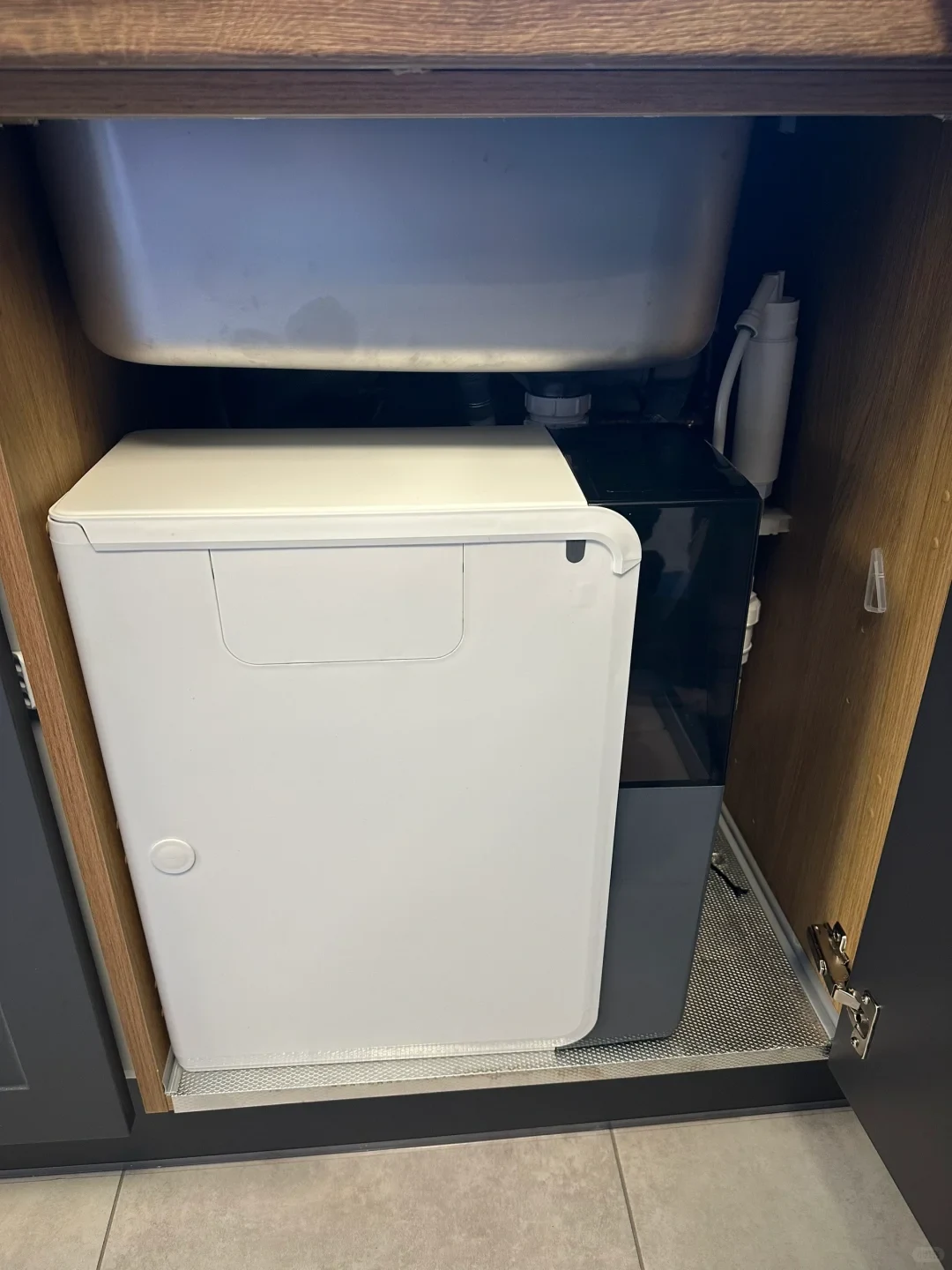 An under-sink cabinet with an installed white and black water purifier appliance located beneath a stainless steel sink.